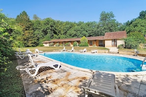 Una piscina con lettini, un portico coperto e un edificio con tetto in tegole.