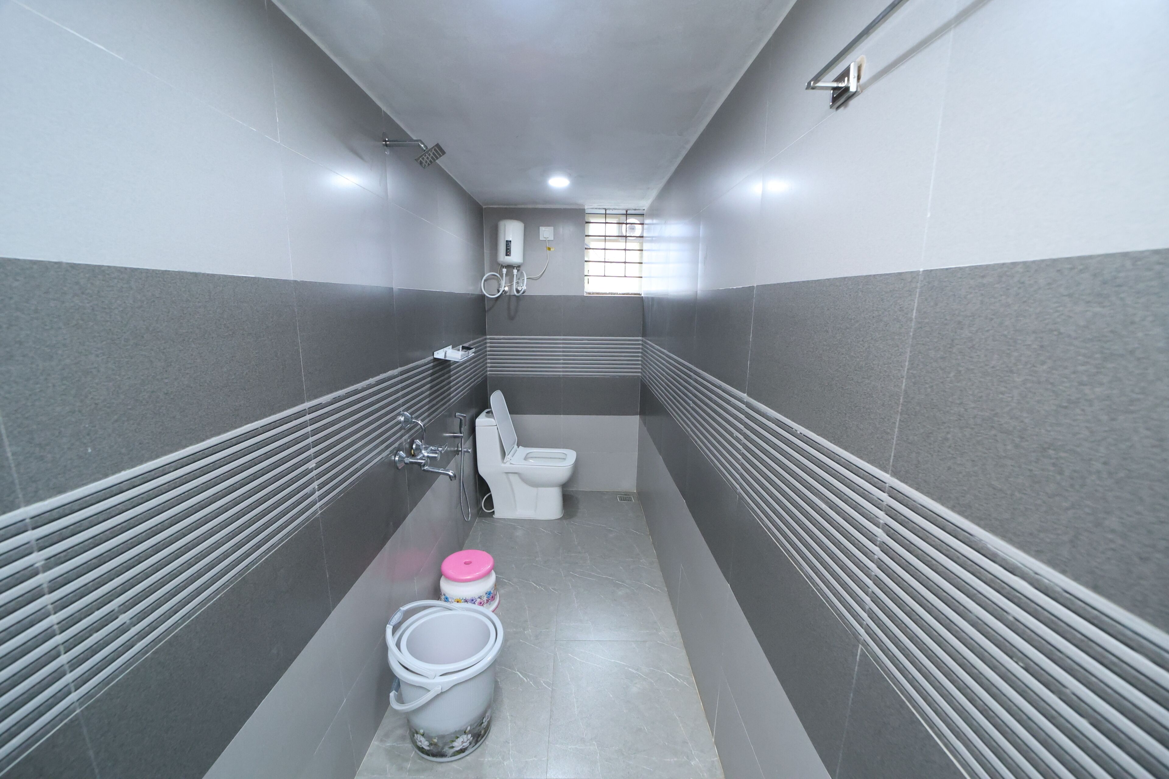 A narrow bathroom with a toilet, a shower, and two buckets.