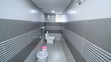 A narrow bathroom with a toilet, a shower, and two buckets.