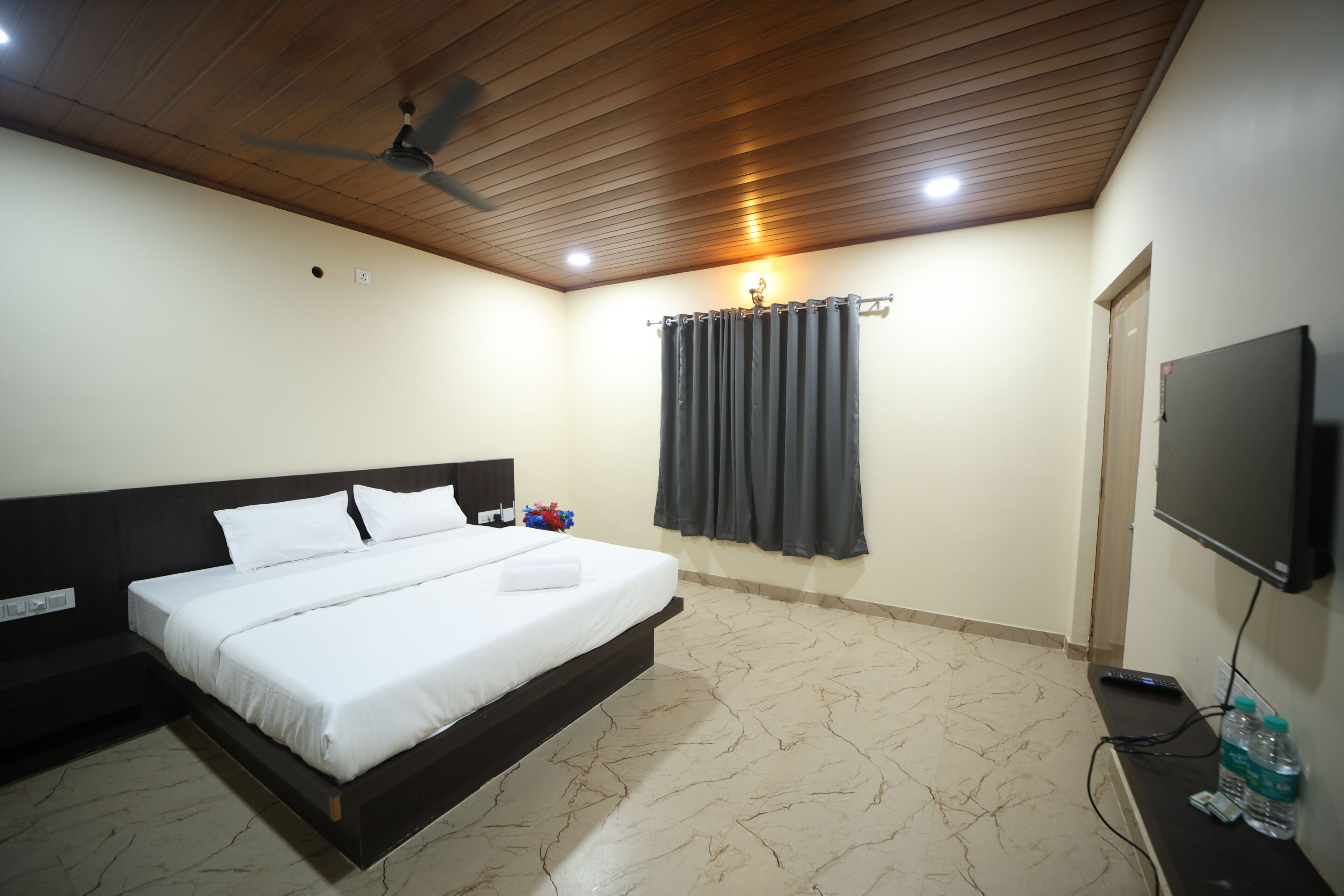 A bedroom with a bed, a ceiling fan, a TV, and a curtain.