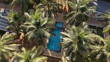 Vista aérea de una piscina rodeada de palmeras, con un diseño de cuadros alrededor de la zona de la piscina.