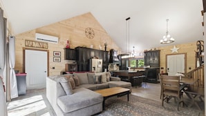 Una sala de estar amplia con un sofá modular grande, techo de madera y un área de cocina con armarios oscuros y una araña.