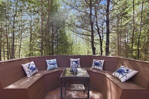 A curved wooden bench with cushions and a small table in a forested area. - Cozy NH Log Home | Ski, Hike & Unwind (Littleton)