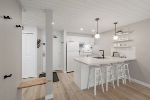Une cuisine moderne avec des meubles blancs, un îlot central doté de tabourets et un éclairage suspendu.