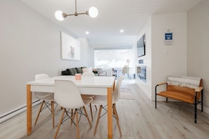 Un espace de salle à manger moderne avec une table et des chaises blanches, un banc et un luminaire suspendu au plafond.