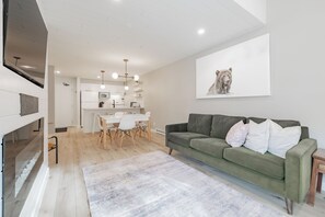 Un salon moderne avec un canapé vert, un tapis blanc et un coin repas comprenant une table et des chaises blanches.