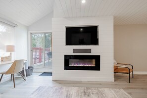 Un salon moderne avec une cheminée, un téléviseur fixé au mur et un coin repas comprenant une table et des chaises.