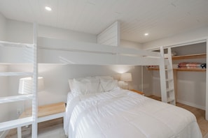 Une chambre avec un lit superposé, une échelle en bois, une table de chevet avec une lampe et une armoire avec des étagères.