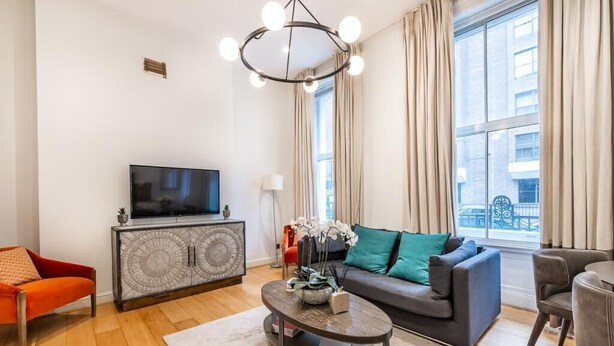 A modern living room with a flat-screen TV, a sofa, a coffee table, and a red chair. - Stylish Marylebone Apartment with Modern Soul (London)