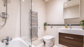 A modern bathroom with a glass-enclosed shower, a white toilet, a wooden vanity, and a mirror above the sink. - Stylish Marylebone Apartment with Modern Soul (London)