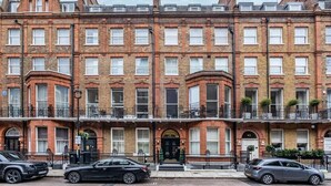 A row of red brick townhouses with multiple stories, each with a front door and a small balcony. - Stylish Marylebone Apartment with Modern Soul (London)