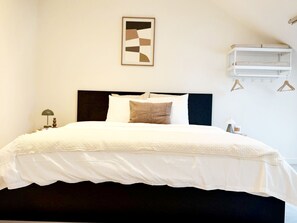 Ein Bett mit dunklem Kopfteil, weißer Bettwäsche, einem einzelnen Kissen und einem Nachttisch mit Lampe.