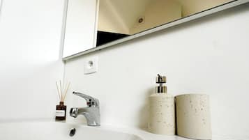 Ein weißes Waschbecken mit chromfarbenem Wasserhahn, ein Spiegel darüber und zwei zylindrische Behälter auf der Ablagefläche.