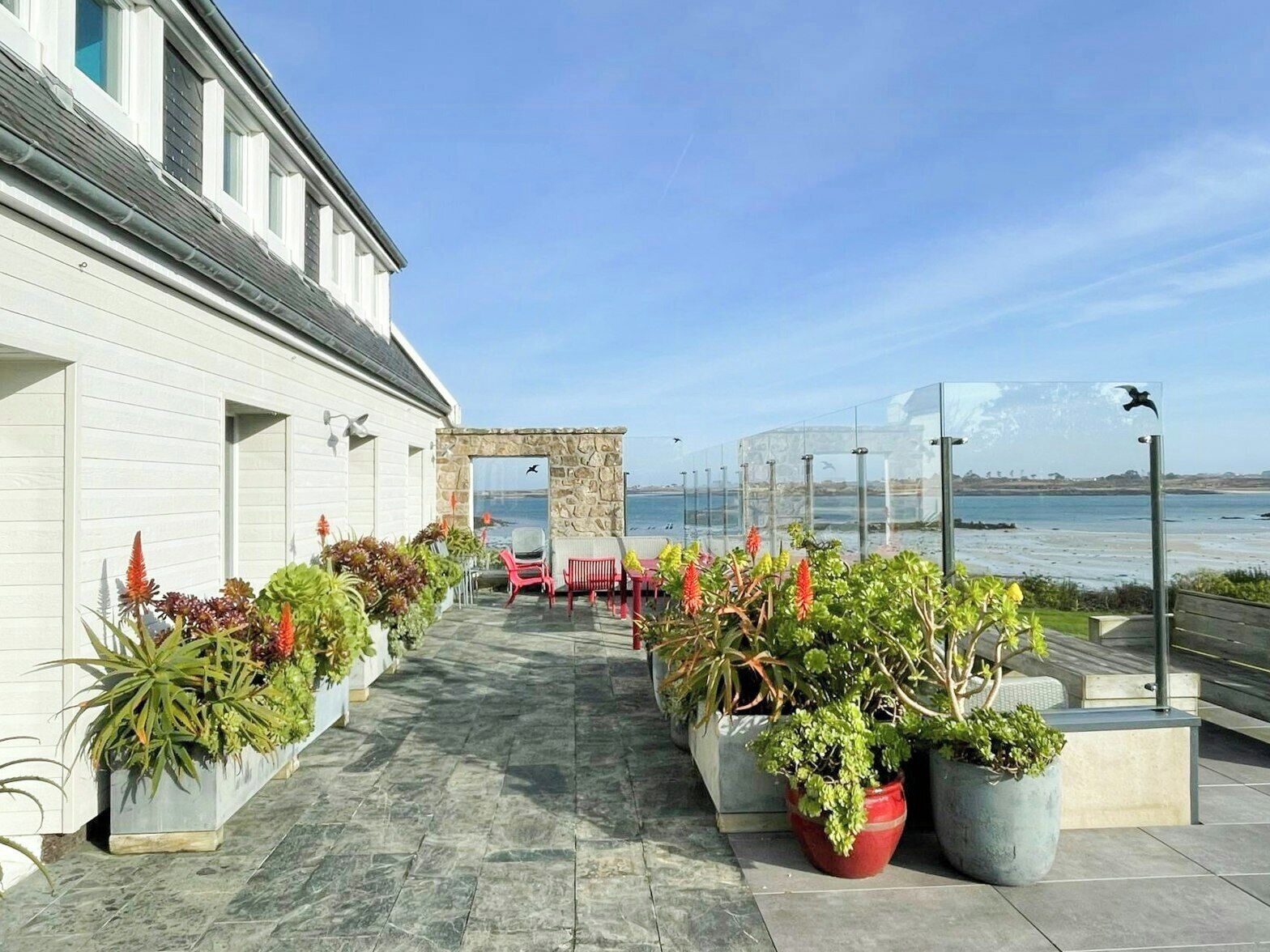 Une terrasse agrémentée de plantes en pot, une arche en pierre et une vue sur la mer.