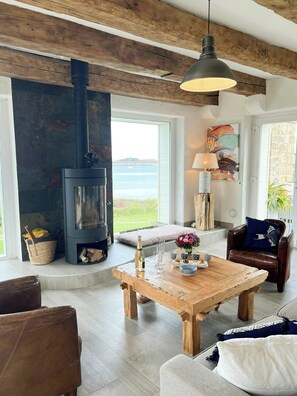 A cozy living room with a fireplace, a wooden coffee table, a leather chair, and a view of the sea. - Beach house with 280-degree sea view in Kergoz (Landeda)