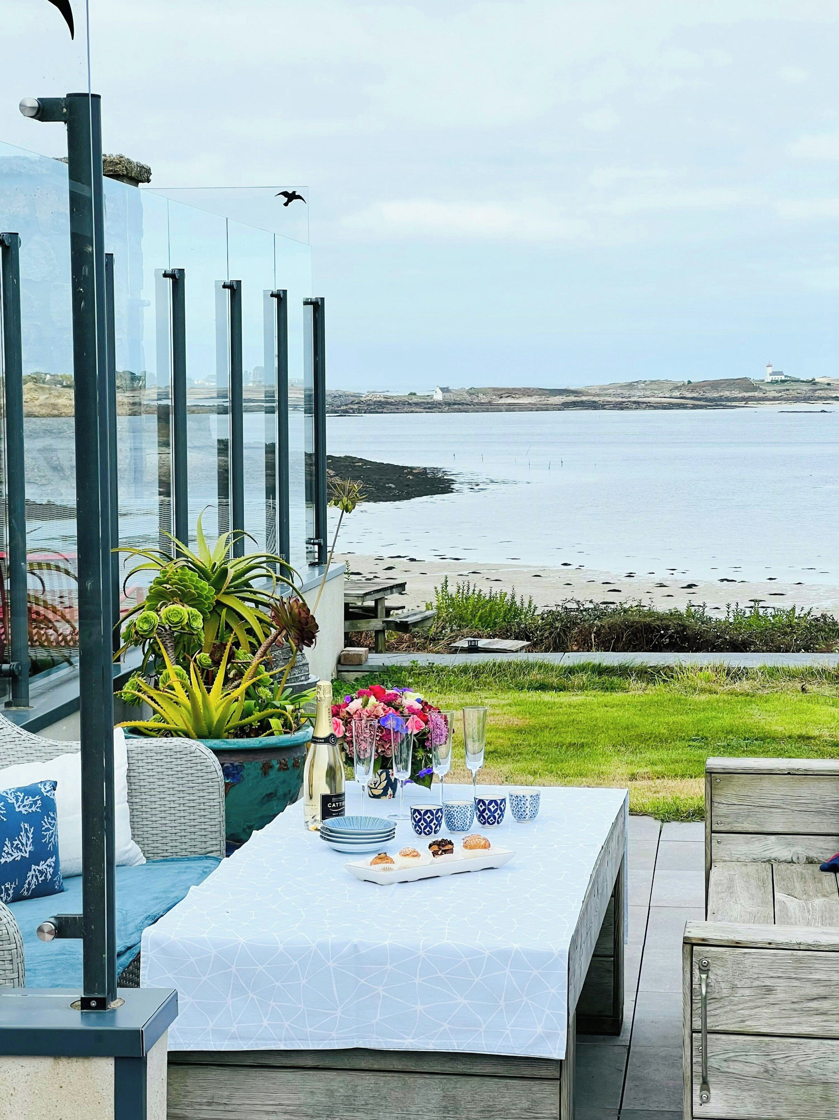 A seaside dining area with a table set for a meal, overlooking the beach and sea.