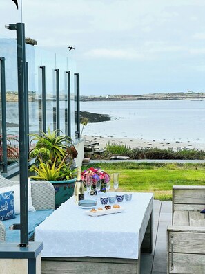 A seaside dining area with a table set for a meal, overlooking the beach and sea. - Beach house with 280-degree sea view in Kergoz (Landeda)