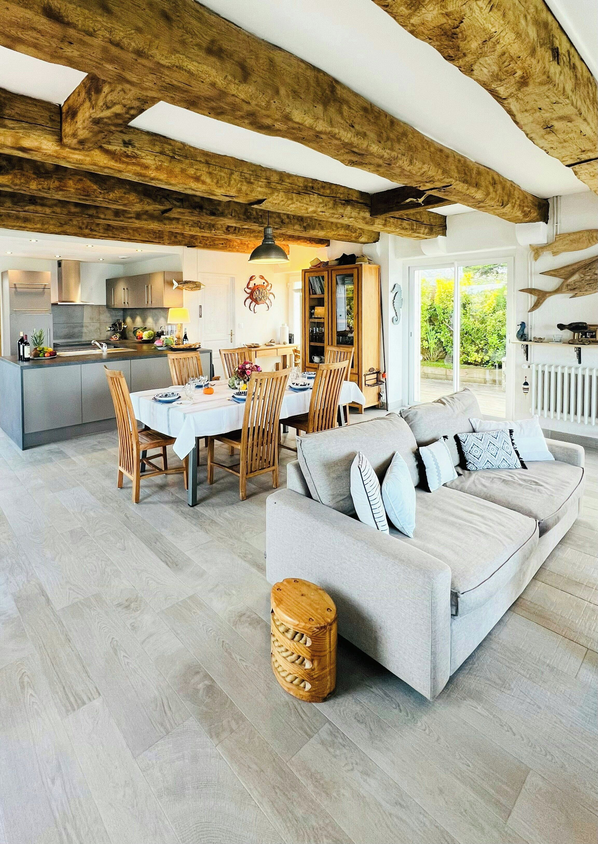 Un grand espace de vie comprenant un canapé et des fauteuils, une table à manger avec des chaises, une cuisine et une vue sur l’extérieur.