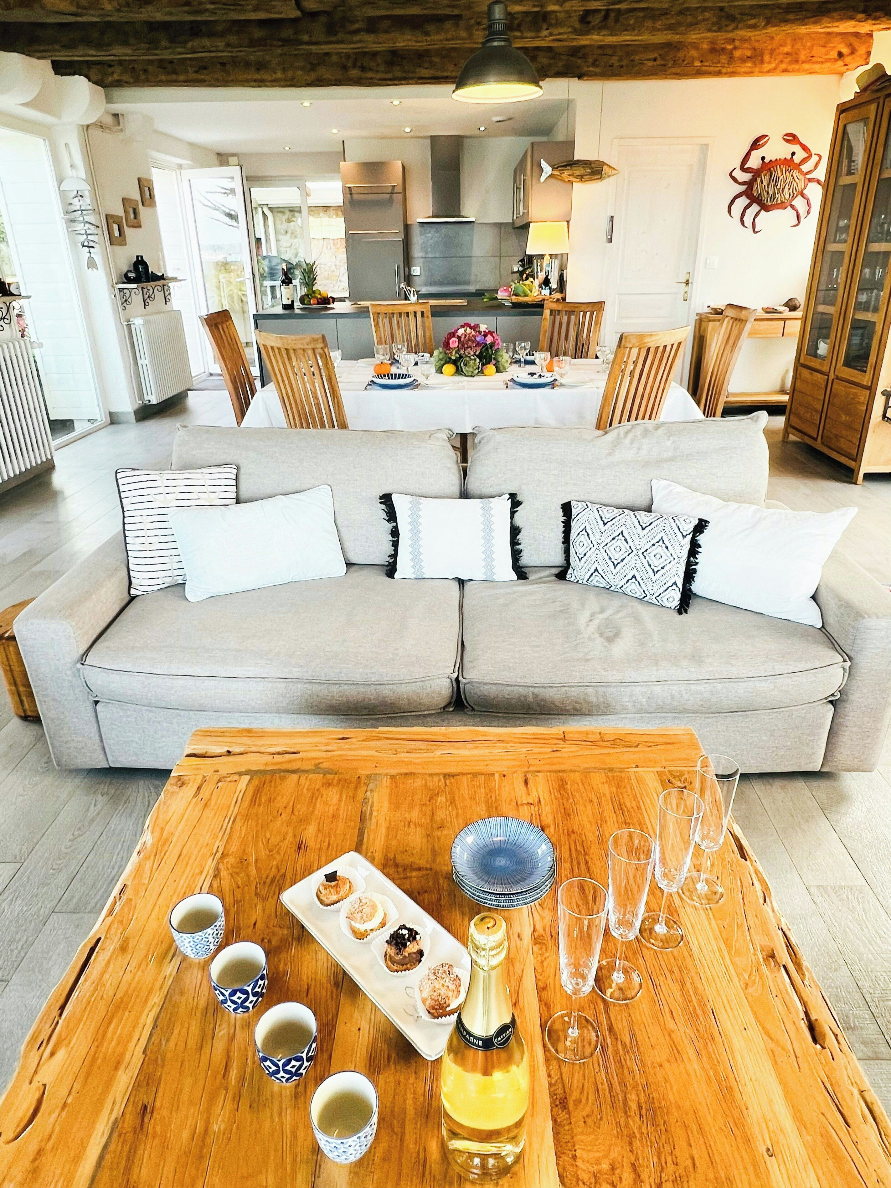 A living room with a sofa, a wooden coffee table with snacks and drinks, and a view into the dining area.