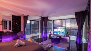 Una habitación de hotel moderna con una cama grande, televisión, escritorio y vistas a la ciudad a través de amplios ventanales.