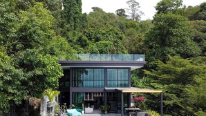 Un edificio moderno de dos pisos con ventanas amplias, rodeado de un bosque denso.