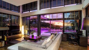 Una sala de estar moderna con un sofá grande, una mesa de centro y un escritorio con una silla. Se ve un jardín y una piscina a través de una ventana amplia.