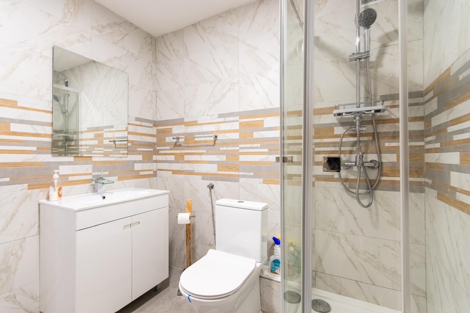 A modern bathroom with a glass-enclosed shower, a white toilet, and a vanity with a mirror.