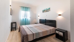 A bedroom with a bed, bedside tables, a nightstand, a window with curtains, and a wall-mounted artwork. - 2 bedroom apartment Praia Da Rocha (Portimão)