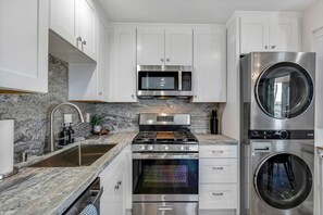 A modern kitchen with stainless steel appliances, white cabinetry, and a granite countertop. - 3BD/3BA | Ocean Views | 1 Block to the Beach (Oceanside)
