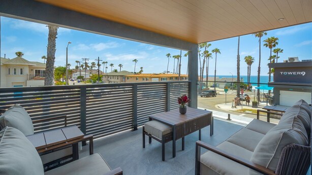 A balcony with a view of the ocean, palm trees, and a sign for 'TOWER9'. - 3BD/3BA | Ocean Views | 1 Block to the Beach (Oceanside)