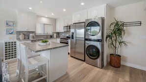 Cocina moderna con armarios blancos, electrodomésticos de acero inoxidable, horno empotrado y una isla central con asientos.