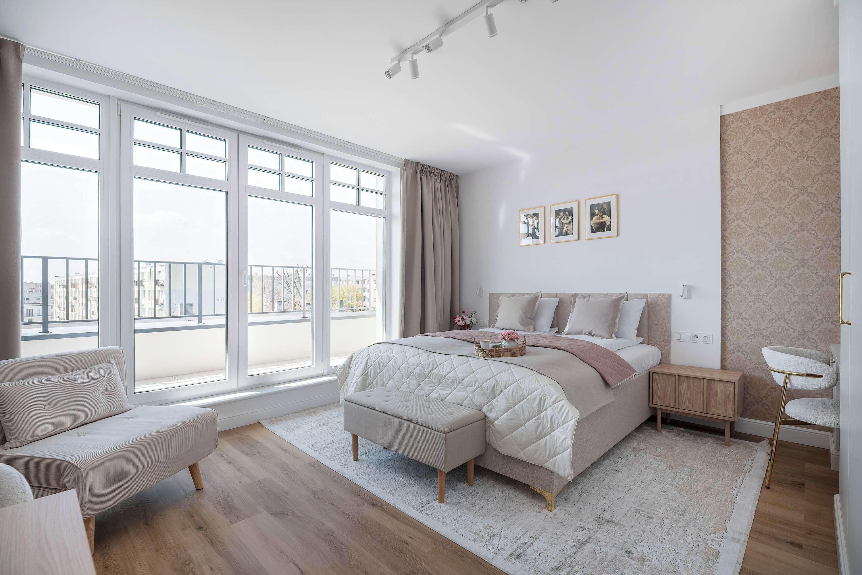A bedroom with a large window, a bed with a quilt, a bedside table, and a chair.