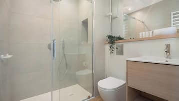 A modern bathroom with a glass-enclosed shower, a toilet, and a wooden vanity with a mirror.