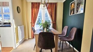 A dining area with a table, chairs, a potted plant, and a view through a window.