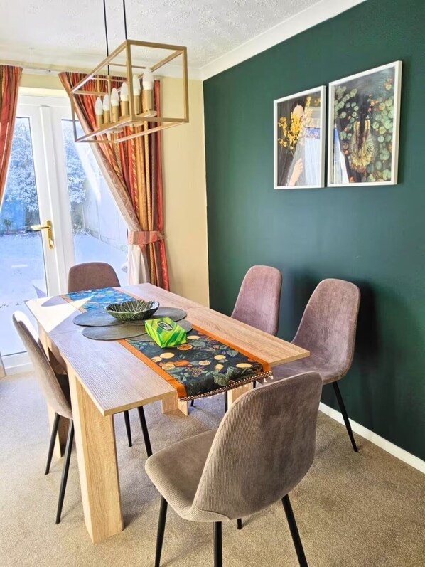 Un comedor con mesa de madera, sillas acolchadas, una lámpara con diseño geométrico y dos cuadros en la pared.