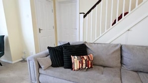A living room with a grey sofa, a staircase with white railings, and two white doors.