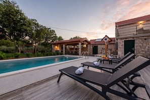 A poolside area with lounge chairs, a covered seating area, and a stone building with a sign. - Villa Zvonimir Zadarvillas (Promina)