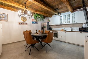 A dining area with a round table and chairs, a chandelier, and a kitchen with white cabinets and stainless steel appliances. - Villa Zvonimir Zadarvillas (Promina)