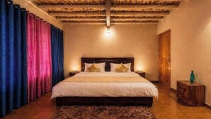 Une chambre avec un lit en bois, une table de chevet, une porte en bois et un plafond avec des poutres apparentes.