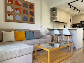 Una sala moderna con un sofá, una mesita de centro de vidrio y una zona de cocina con barra.