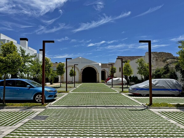 Un estacionamiento con superficie verde estampada, un coche azul y un vehículo cubierto.