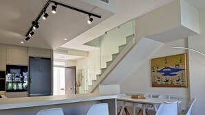 Eine moderne Küche mit einem eingebauten Kühlschrank, ein Essbereich mit weißen Stühlen und eine Treppe, die zu einer anderen Ebene führt.