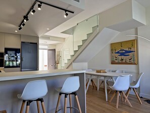 Een moderne keuken met een geïntegreerde koelkast, een eetgedeelte met witte stoelen, en een trap naar een hoger niveau.