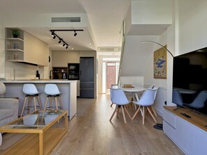 Een moderne keuken met een centraal eiland, barstoelen, een eettafel met stoelen, een flatscreen televisie en een groot raam.