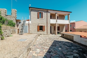Un edificio de piedra con una escalera que lleva a un balcón, un patio empedrado y un muro de piedra.