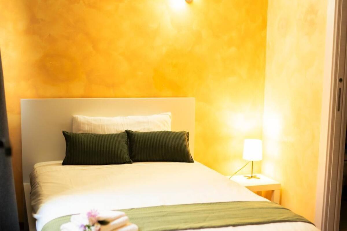 Una habitación de hotel con cama, mesita de noche, lámpara y aire acondicionado.