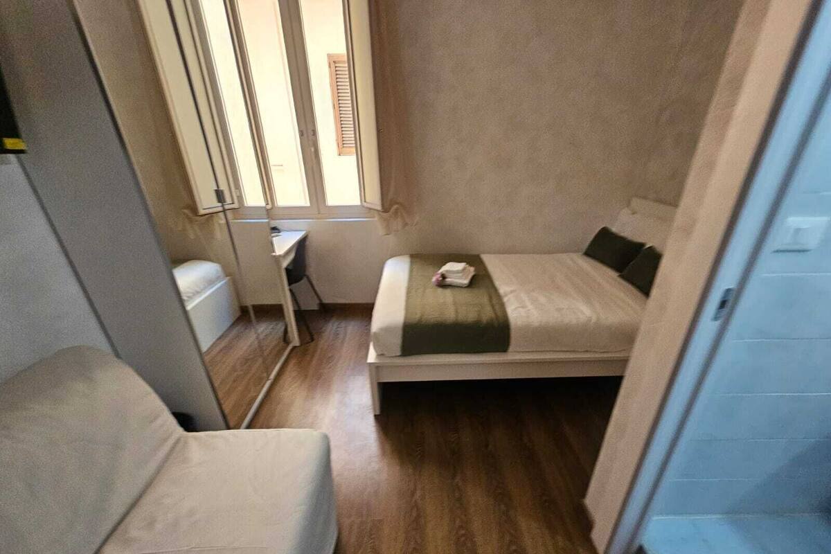 Una habitación pequeña y estrecha con una cama, una silla, un escritorio y una ventana.