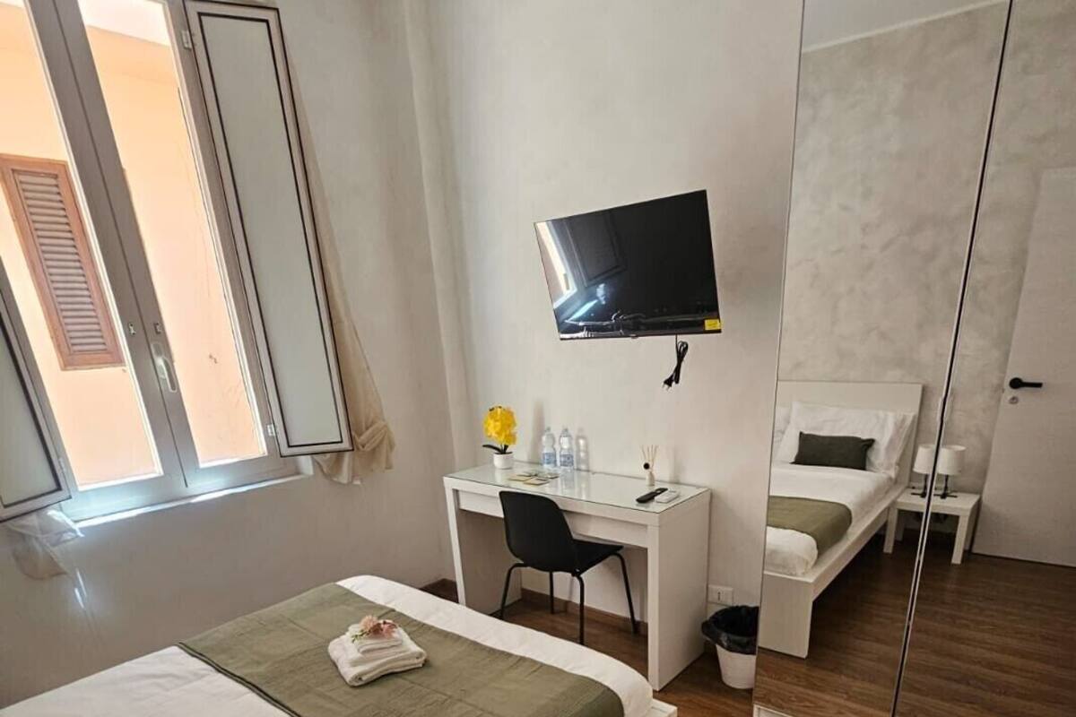 Una habitación de hotel con cama, escritorio, televisor, espejo y ventana.