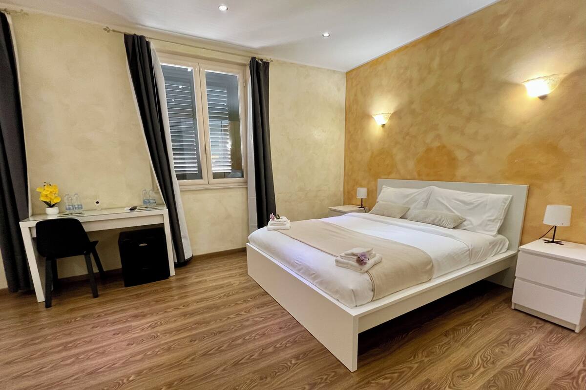 Una habitación de hotel con cama, escritorio, silla y ventana con cortinas.