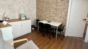 Een compacte kamer met een kitchenette, een eethoek met tafel en stoelen, een comfortabele bank en een wandairconditioner.